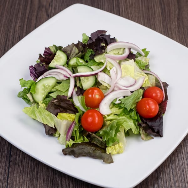 Fresh garden salad with mixed greens, sliced cucumbers, red onions, and cherry tomatoes on a white plate.
