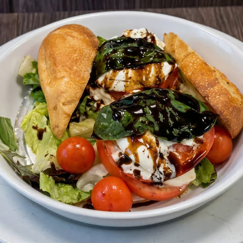 Caprese salad with fresh mozzarella, sliced tomatoes, basil, balsamic glaze, and baguette slices.