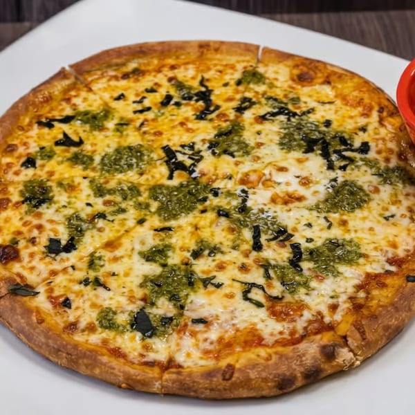 A whole, sliced pesto pizza with melted cheese and dark green basil on a white plate.